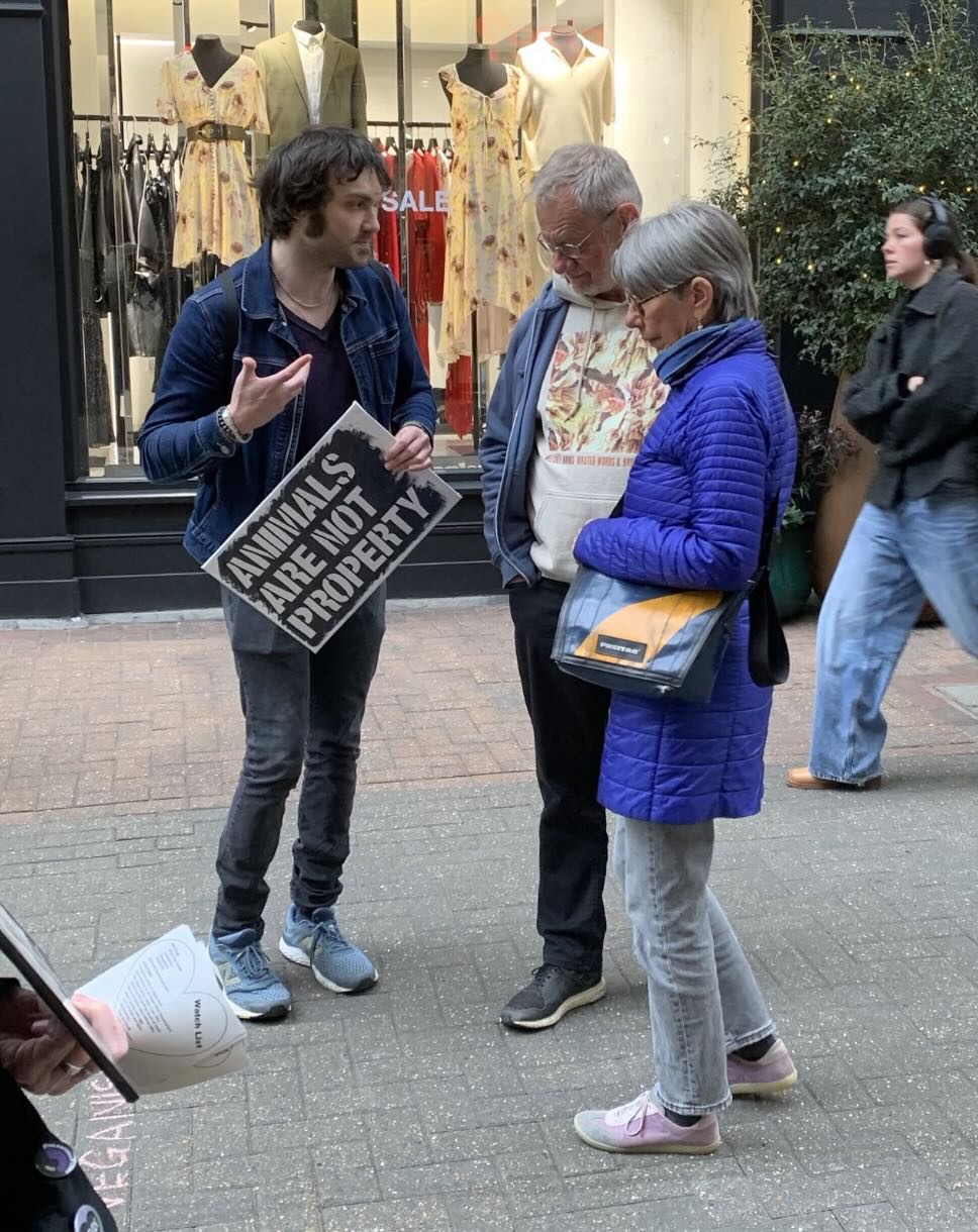 A volunteer holding an 'Animals are not property' sign in conversation with two passers-by